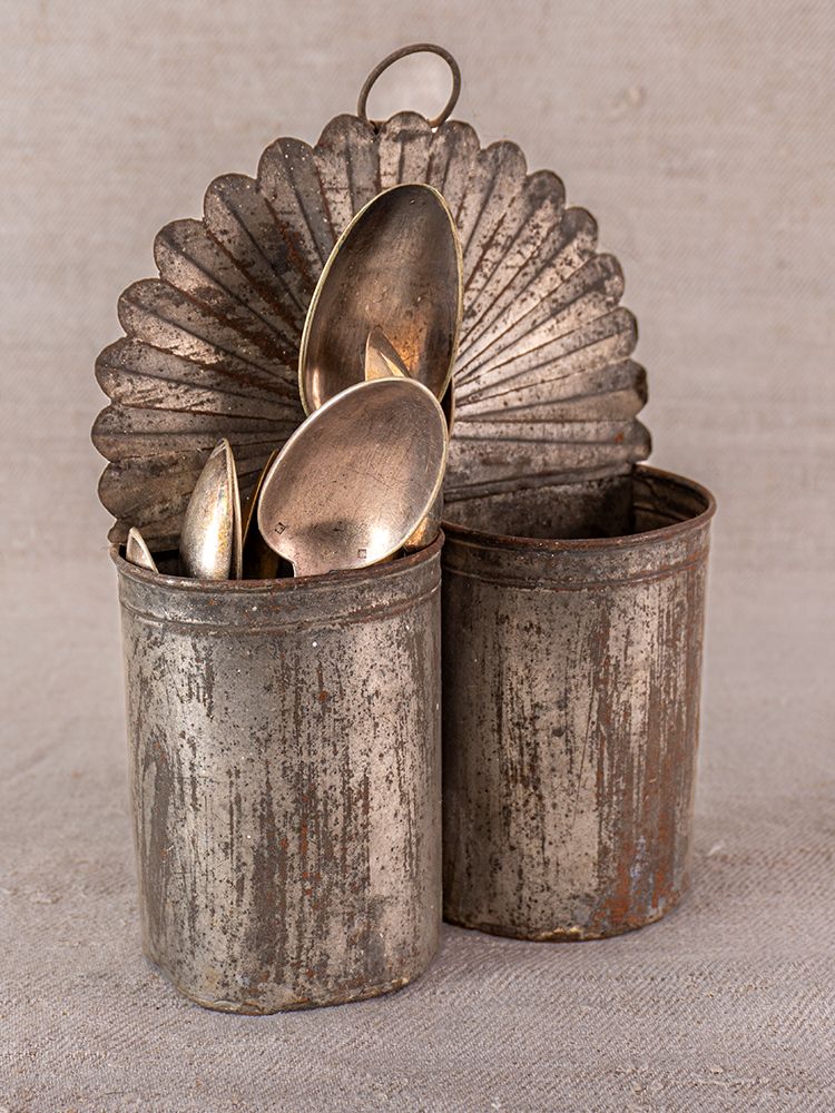 Provence wall-mounted aged steel utensil holder with silver spoons, ornate fan detail, on beige fabric backdrop.