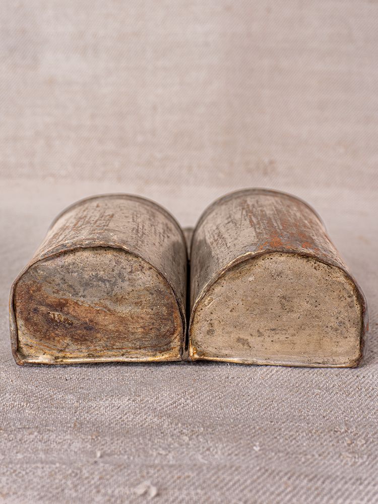 Pair of aged steel Provençal wall mounted utensil holders with weathered rectangular forms and rounded tops on textured fabric.