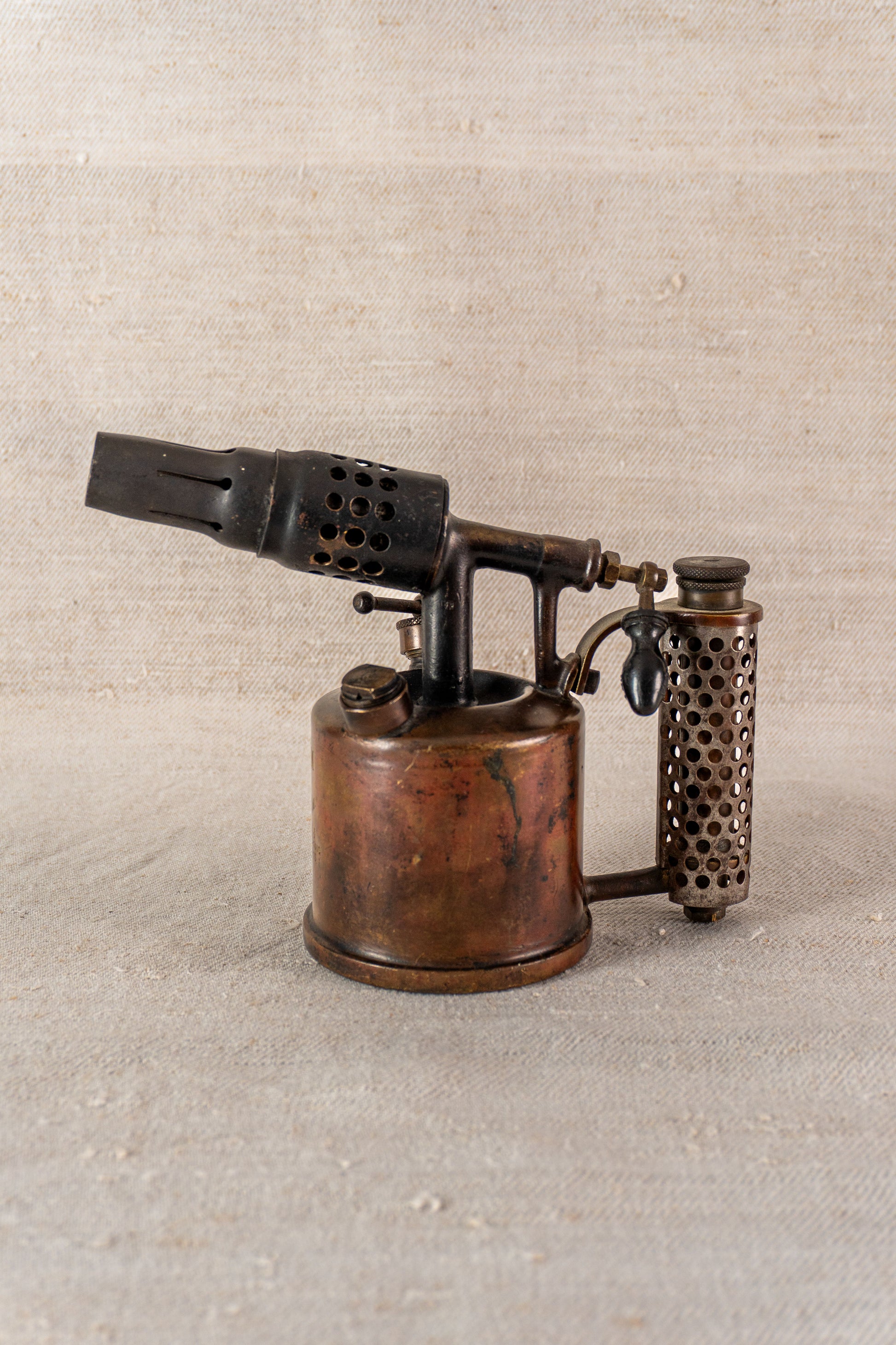 Vintage French Vesta F.J. Paris blowtorch, circa 1920, with cylindrical body and side handle on neutral textured surface.