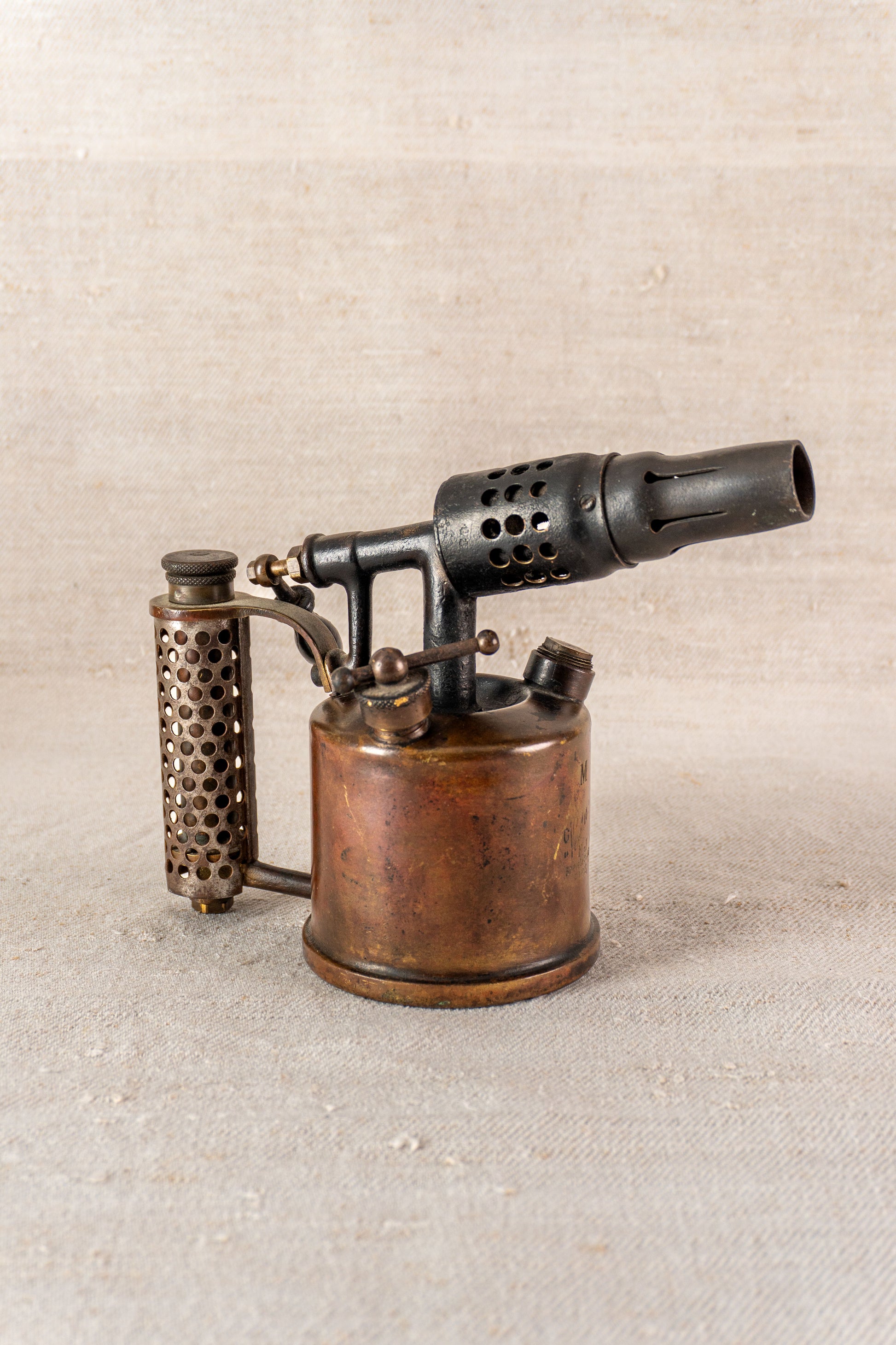 Vintage French Vesta F.J. Paris blowtorch, perforated handle and black nozzle, displayed on neutral textured fabric.