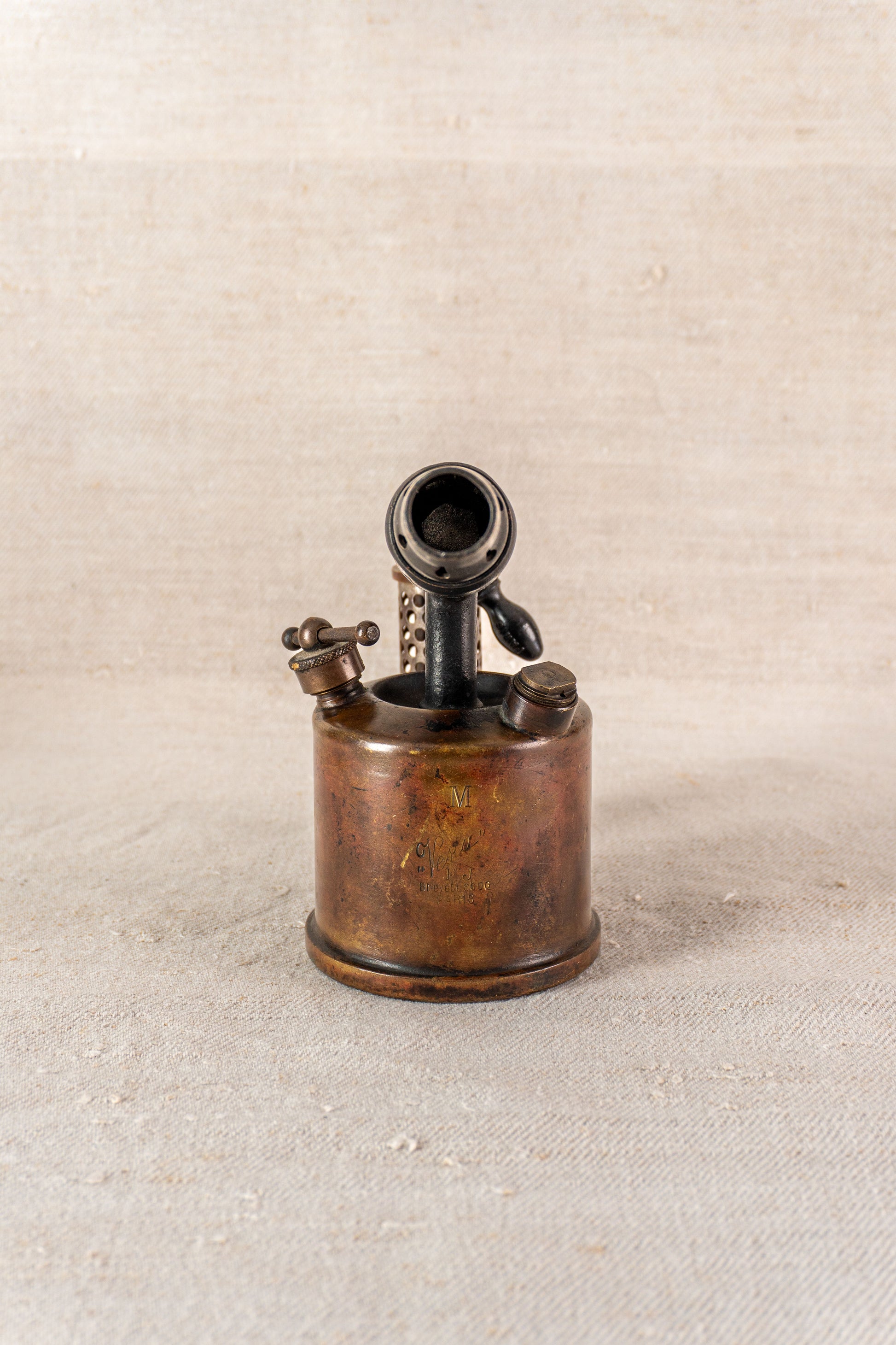 Vintage French blowtorch by Vesta F.J. Paris circa 1920, round fuel tank, upright on beige textured surface.