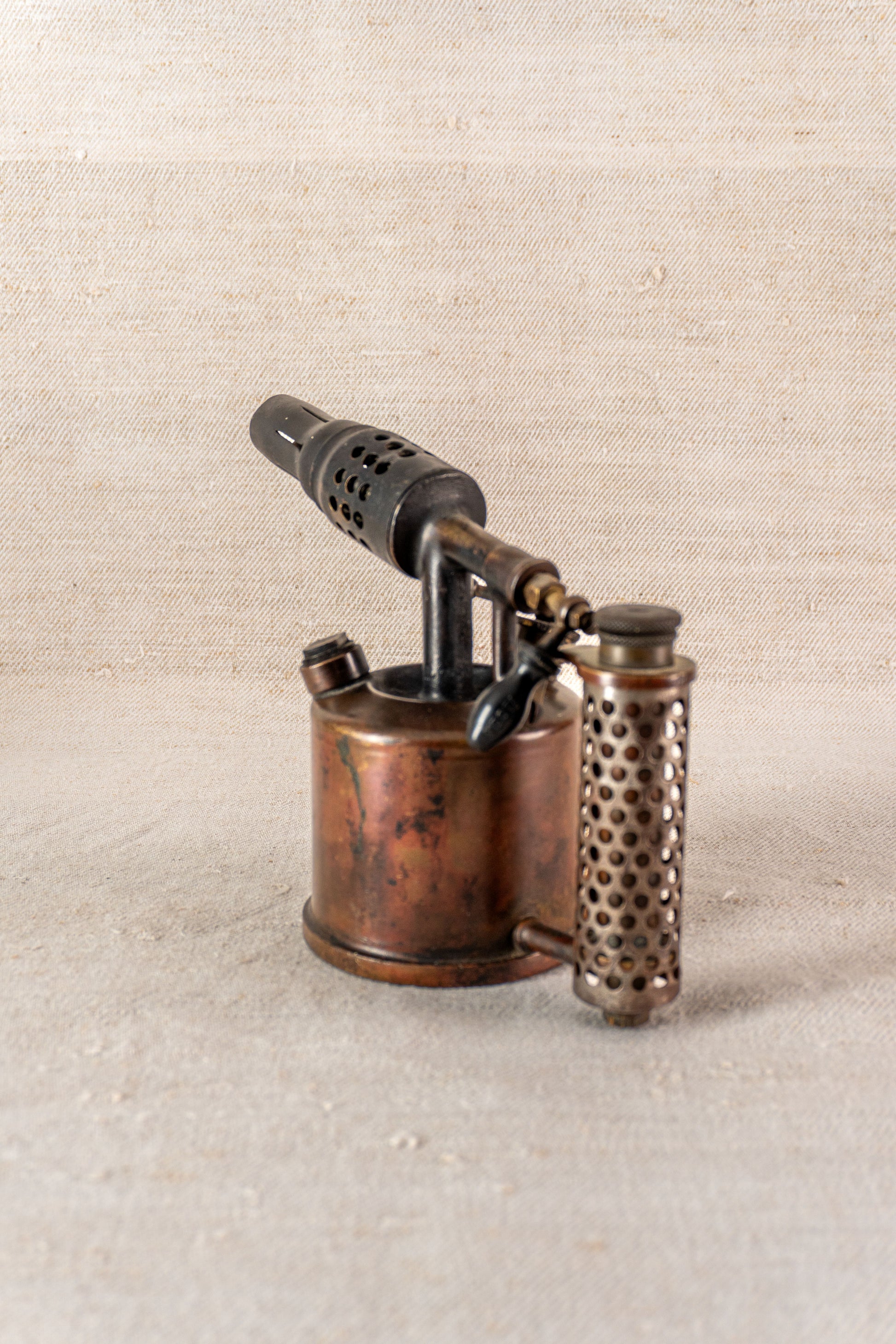 Vintage French Vesta F.J. Paris blowtorch, circa 1920, cylindrical metal body and perforated handle on light textured surface.