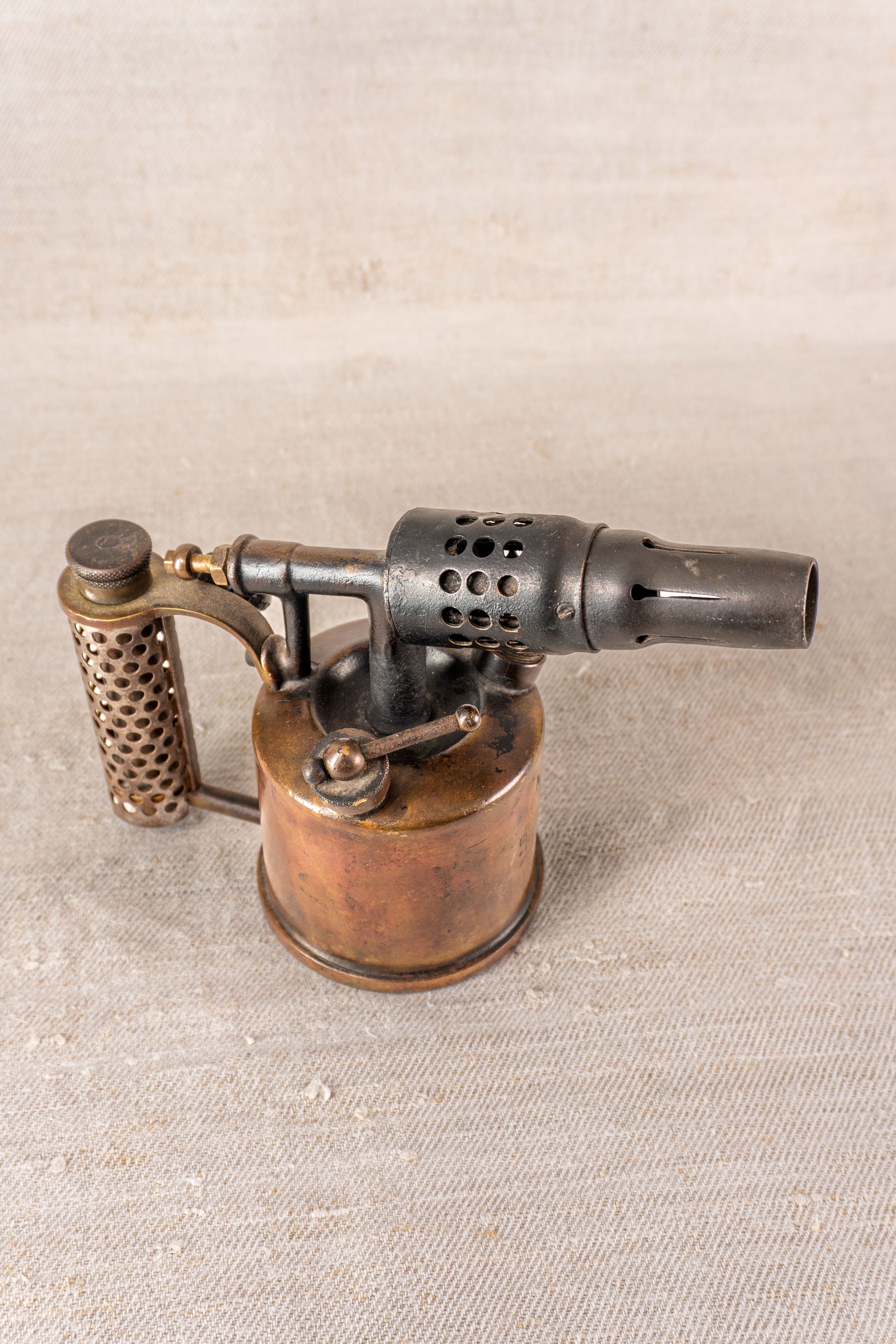 Vintage French Vesta F.J. Paris blowtorch, c.1920, brass tank and vented nozzle on textured beige backdrop.