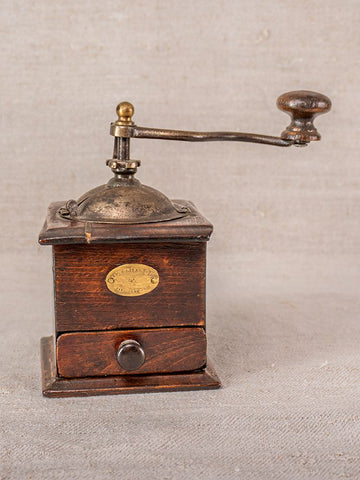 Antique French Peugeot Frères coffee grinder with metal crank handle and front drawer on a textured neutral surface.