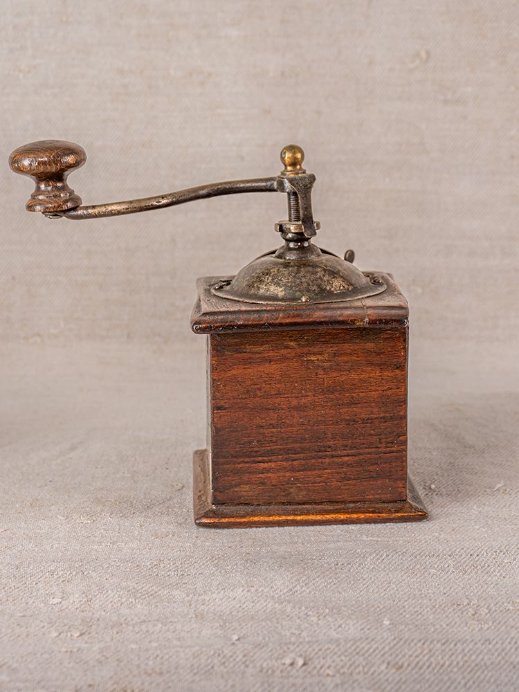 Antique French Peugeot Frères coffee grinder with wooden box base and metal crank, on neutral fabric background.