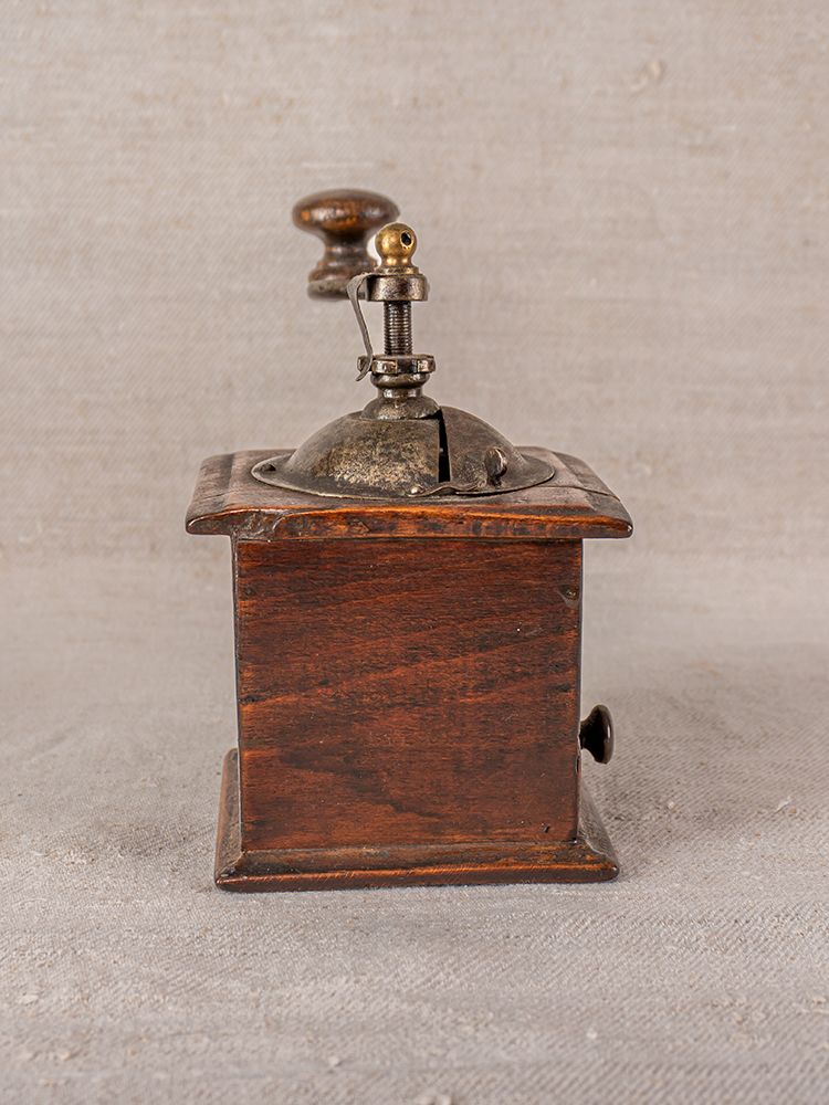 Antique French Peugeot Frères coffee grinder with wooden box base, metal grinder, and crank on neutral fabric background.