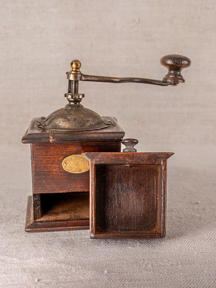 Antique French Peugeot Frères coffee grinder with wooden body, metal crank, and open drawer on a neutral background.