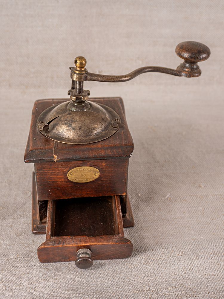 Antique Peugeot Frères French coffee grinder in dark wood and metal with crank handle on textured grey surface.