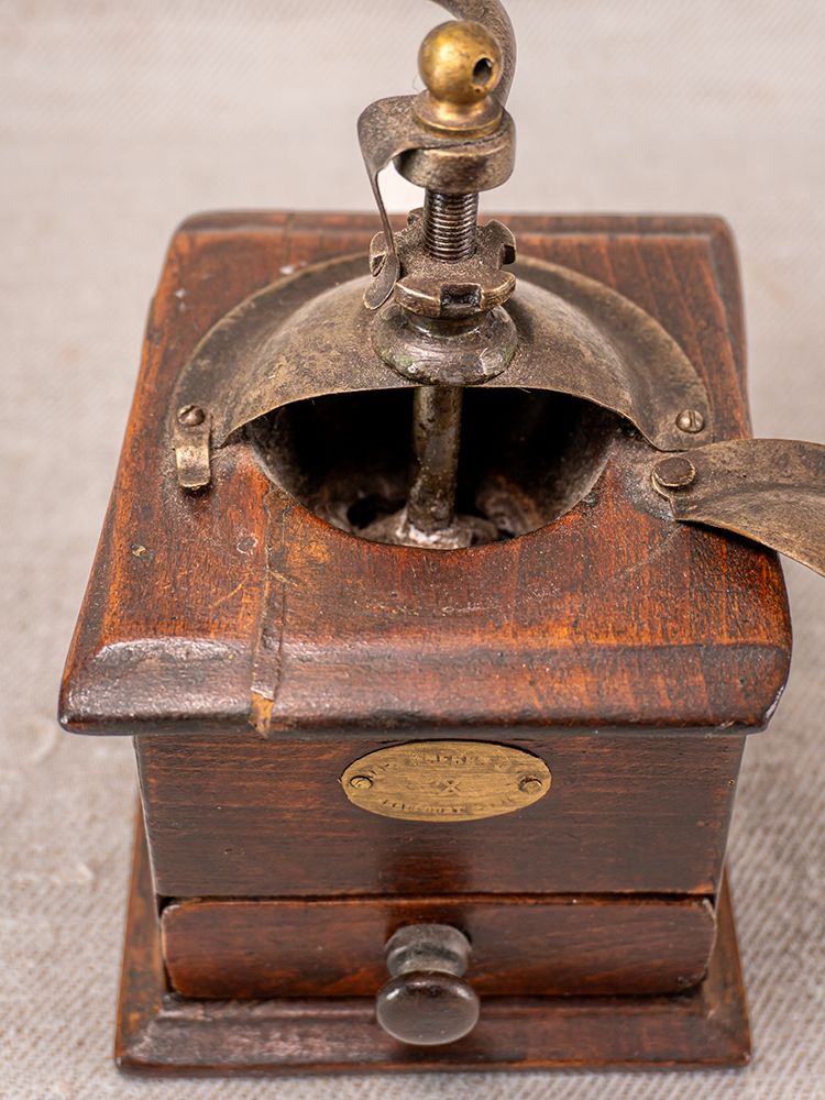Antique French Peugeot Frères coffee grinder with metal handle, brass accents, and aged oak body on textured surface.