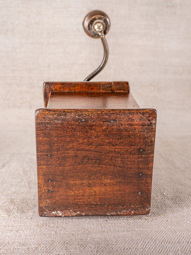 Antique French Peugeot Frères coffee grinder with oak base and metal handle, on neutral fabric background.