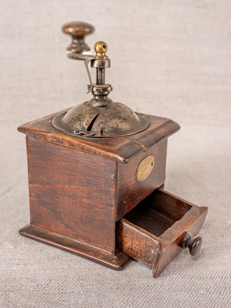 Antique French Peugeot Frères coffee grinder with metal handle and dome, open drawer, on neutral fabric background.