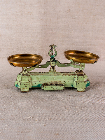 Vintage French JEP toy balance scale in green cast iron and brass on beige textured fabric.