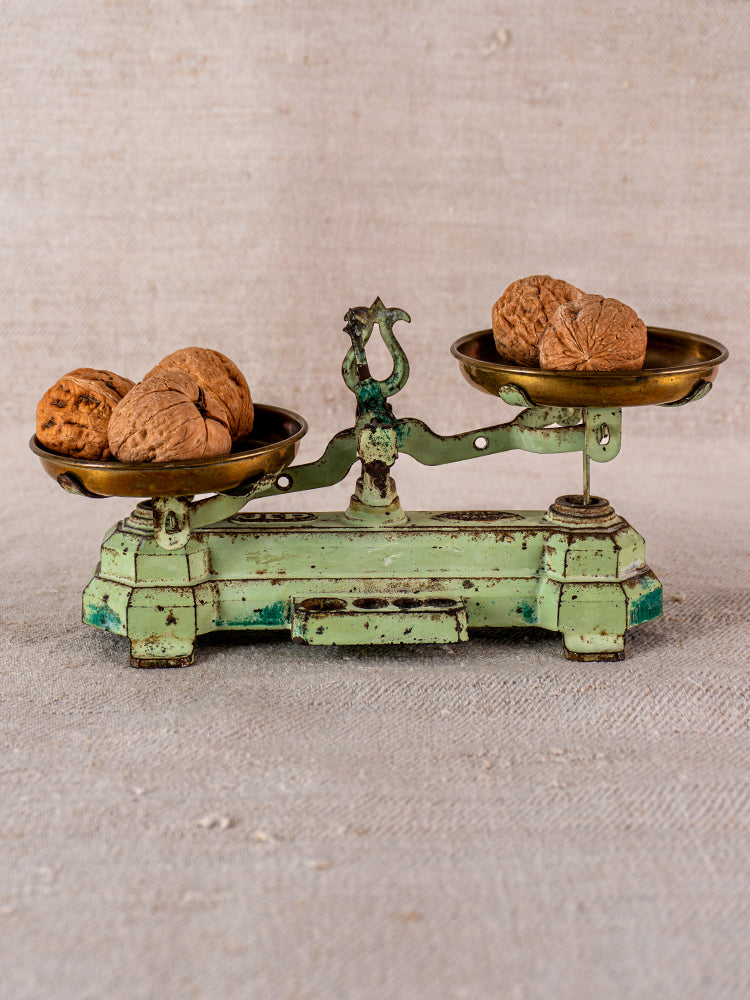 Vintage French JEP toy balance scale in green cast iron and brass with walnuts, on beige textured surface.