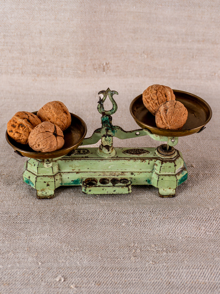 Vintage French JEP cast iron and brass toy balance scale with walnuts, on textured beige surface.
