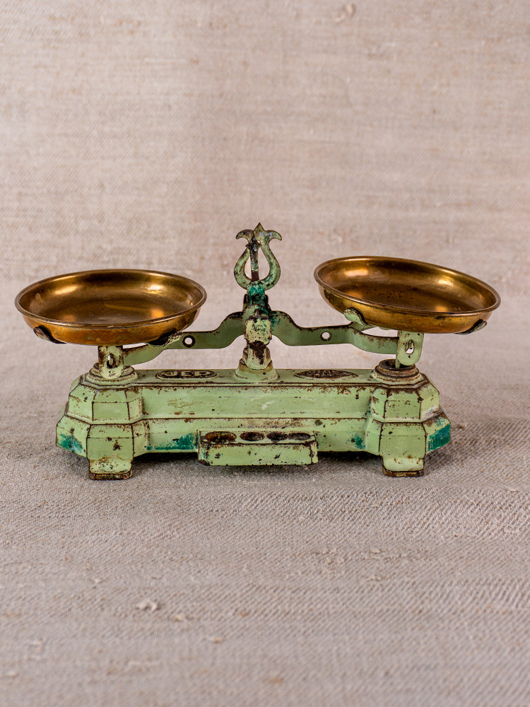 Vintage French JEP toy balance scale in green cast iron with two brass trays on beige fabric.