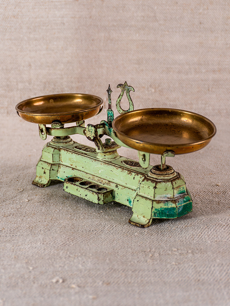 Vintage French JEP cast iron toy balance scale with two brass pans on a beige textured surface.