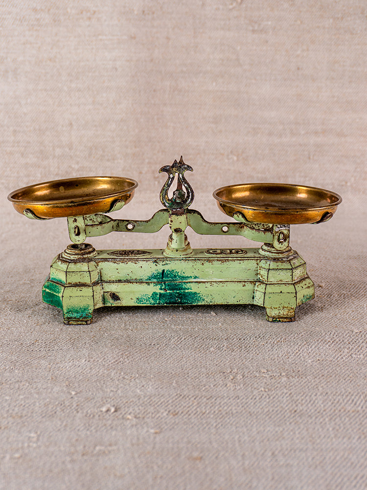 Vintage French JEP toy balance scale in green cast iron with brass pans on neutral fabric.