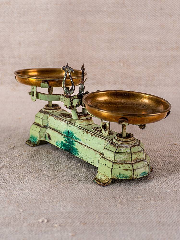 Vintage French JEP toy balance scale in green cast iron with brass pans on beige fabric surface.