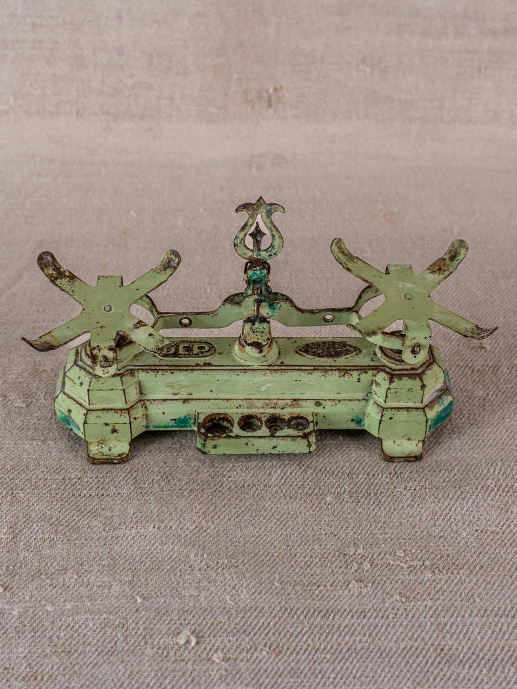 Vintage French JEP toy balance scale in green cast iron and brass with ornate detailing on beige fabric.