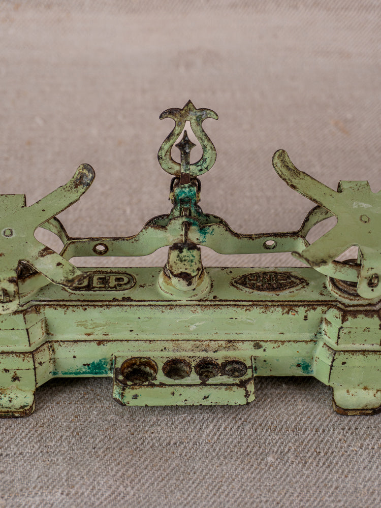 Vintage French JEP toy balance scale in green cast iron with brass accents, worn patina, on fabric background.