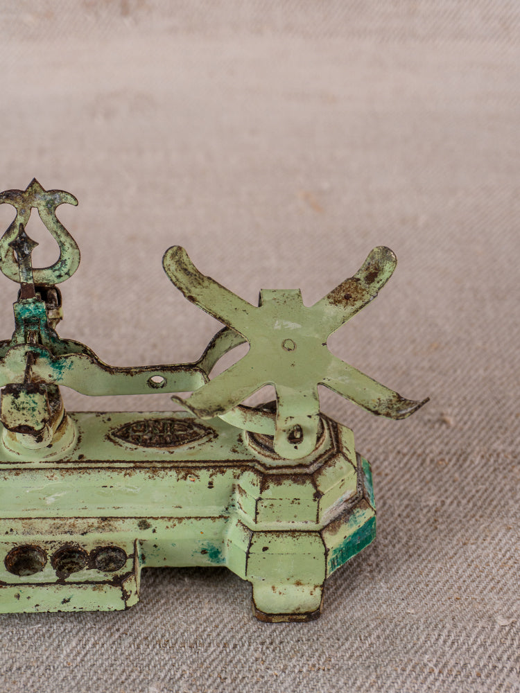 Vintage French JEP toy balance scale in green cast iron with brass accents, weathered finish, on beige fabric.