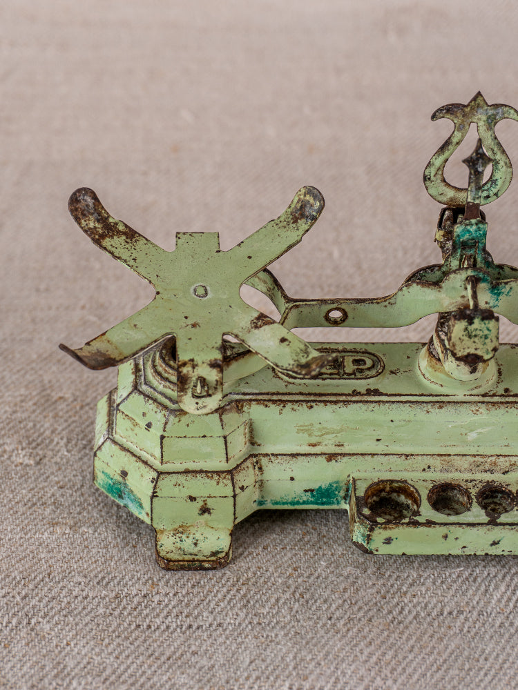 Antique French JEP toy balance scale in green cast iron and brass with rusted patina on beige textured fabric.
