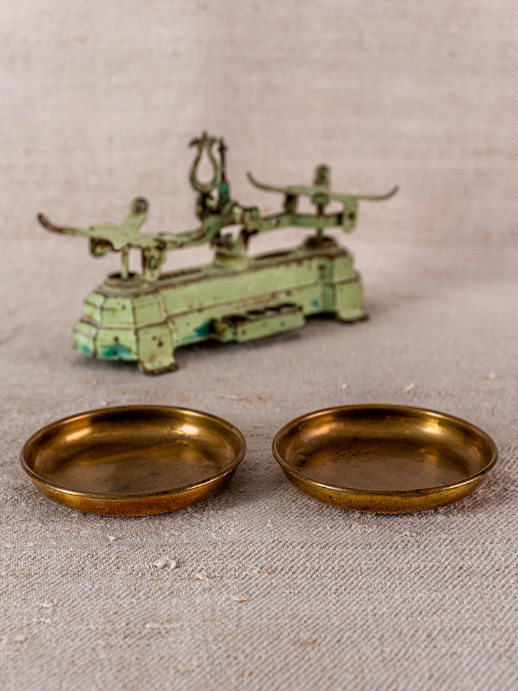 Vintage French JEP toy balance scale in green cast iron with brass weighing pans on beige surface.