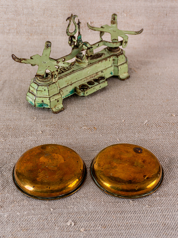 Vintage French JEP green cast iron toy balance scale with brass weighing pans on beige textured fabric.