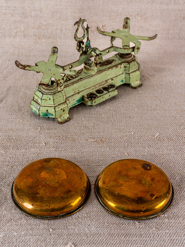 Vintage French JEP toy balance scale in green cast iron and brass with two gold weighing pans on beige surface.