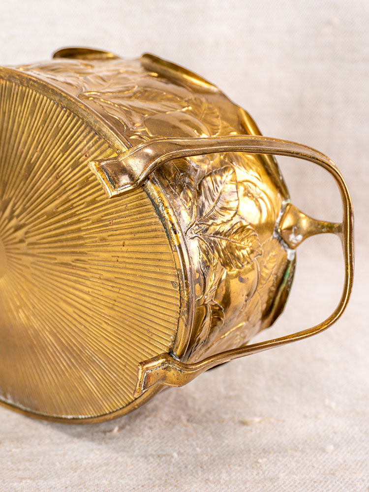 Vintage Swiss brass jardinière with embossed fruit motif and handle, displayed on light fabric in mid-century style.