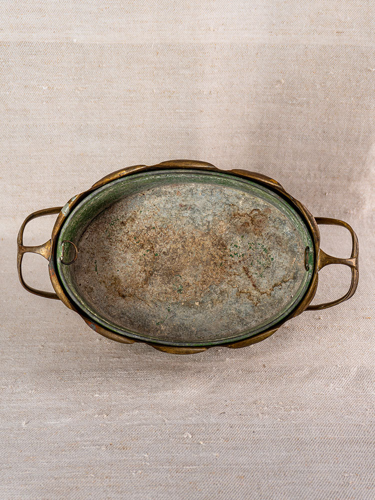 Vintage Swiss brass jardinière with embossed fruit motif and dual handles, mid-century style, on textured beige fabric.