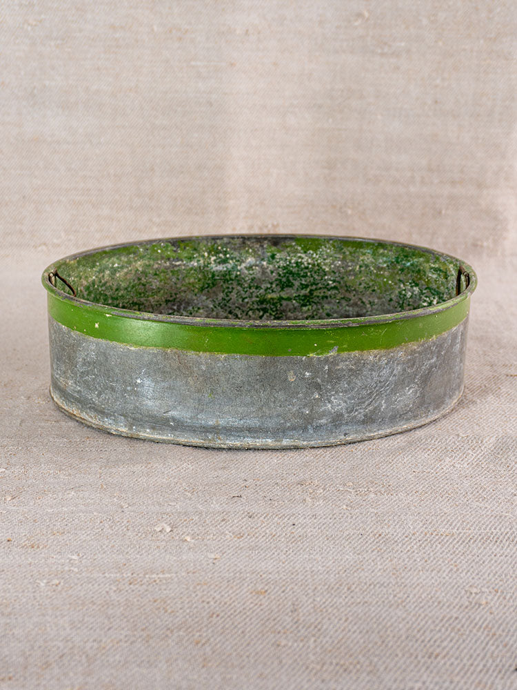 Vintage Swiss brass jardinière with embossed fruit motifs, round shallow form, green rim, on textured beige fabric.