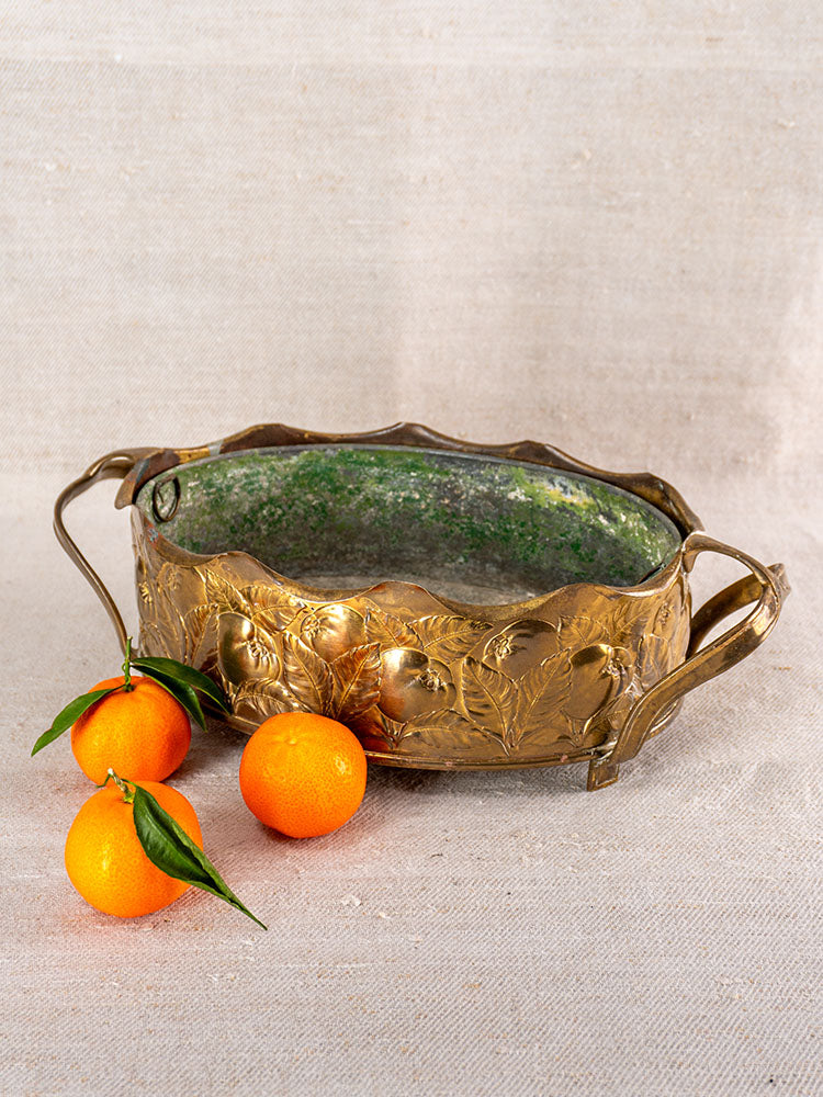 Vintage Swiss brass jardinière with embossed fruit motif, displayed beside fresh mandarins on a textured beige surface.