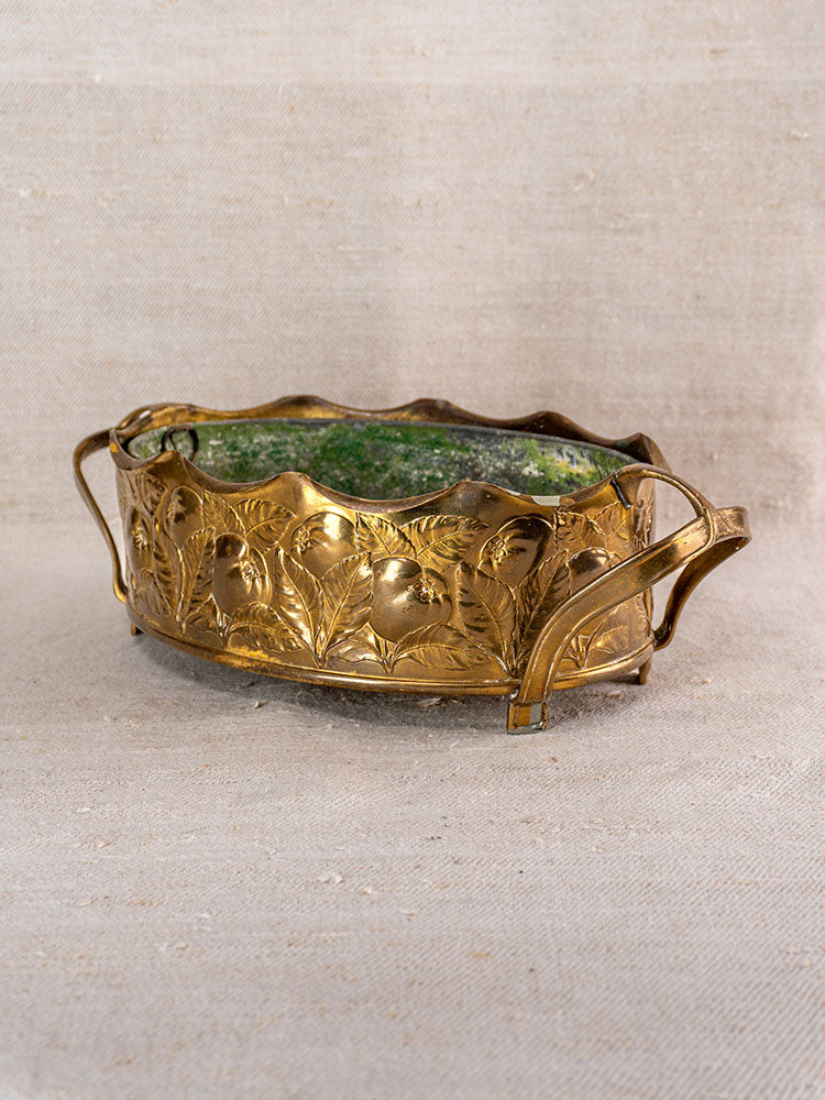 Vintage Swiss brass jardinière with embossed fruit motif and curved handles, mid-century, on neutral fabric background.