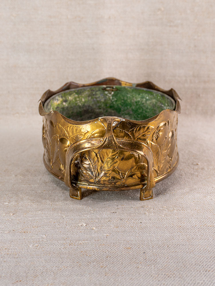Vintage Swiss brass jardinière with embossed fruit motif and mid-century design on textured beige fabric background.
