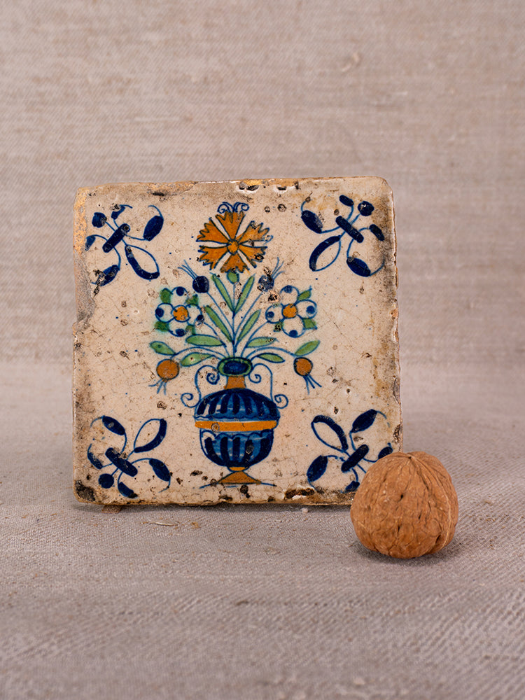 17th-century French faience tile from Provence with hand painted floral bouquet, blue vase, and corner motifs, on beige fabric.
