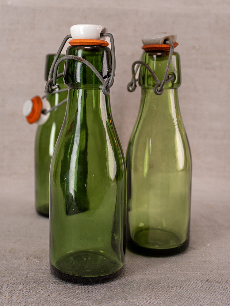 Set of three Swiss Bülach green glass clamp bottles with porcelain tops on a light textured surface.