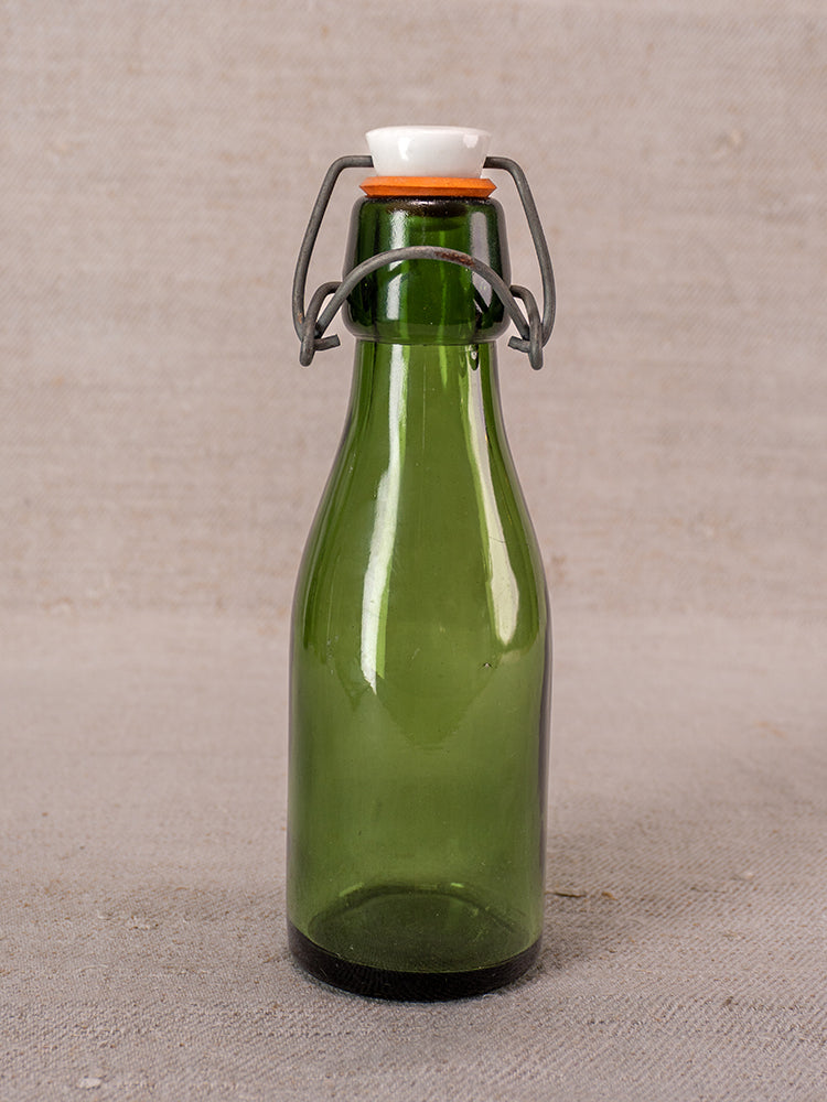 Set of three Swiss Bülach green glass clamp bottles with porcelain tops displayed on beige fabric.