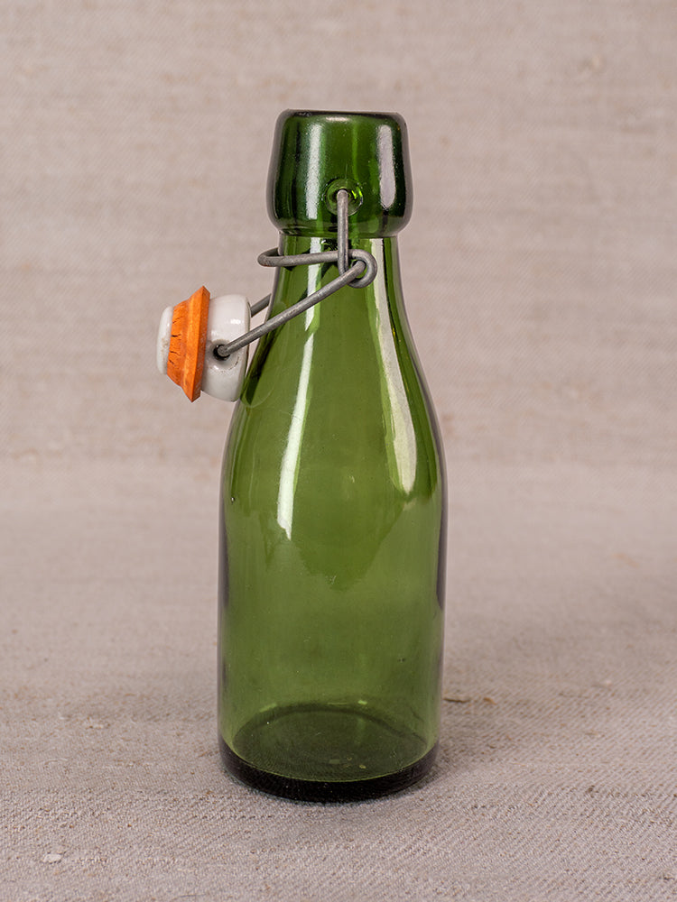 Set of three Swiss Bülach green glass clamp bottles with porcelain tops on a neutral textured surface.