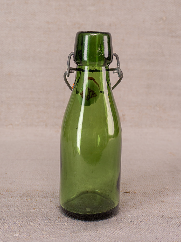 Set of three Swiss Bülach green glass clamp bottles with porcelain tops on a neutral fabric backdrop.