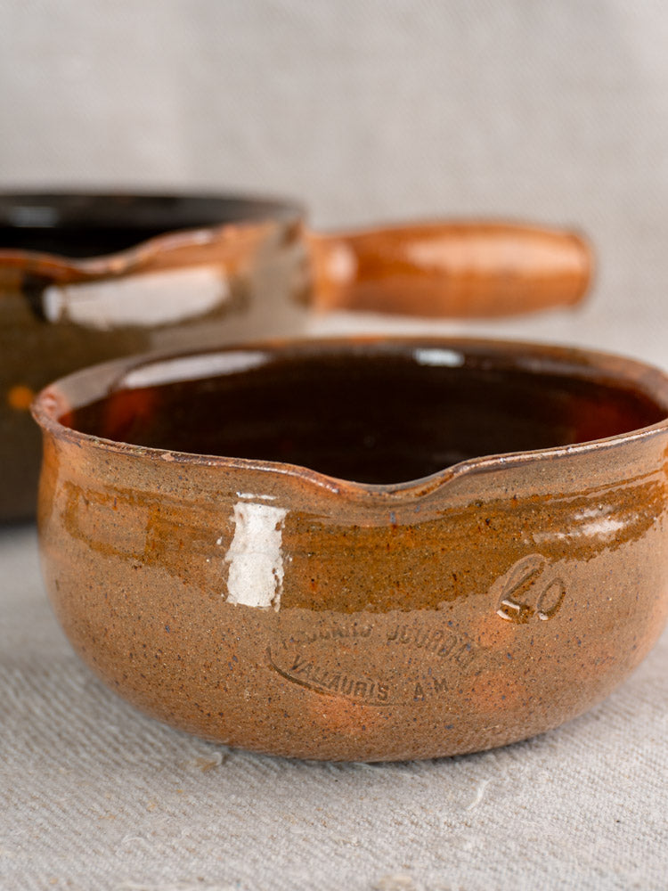 Pair of mid-century French Grandjean Jourdan Vallauris poêlon bowls, rustic brown, on textured fabric background.
