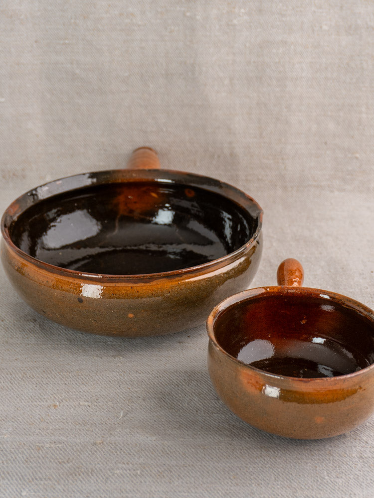 Pair of Grandjean Jourdan Vallauris antique French poêlons with brown and dark glossy glaze on beige textured fabric.