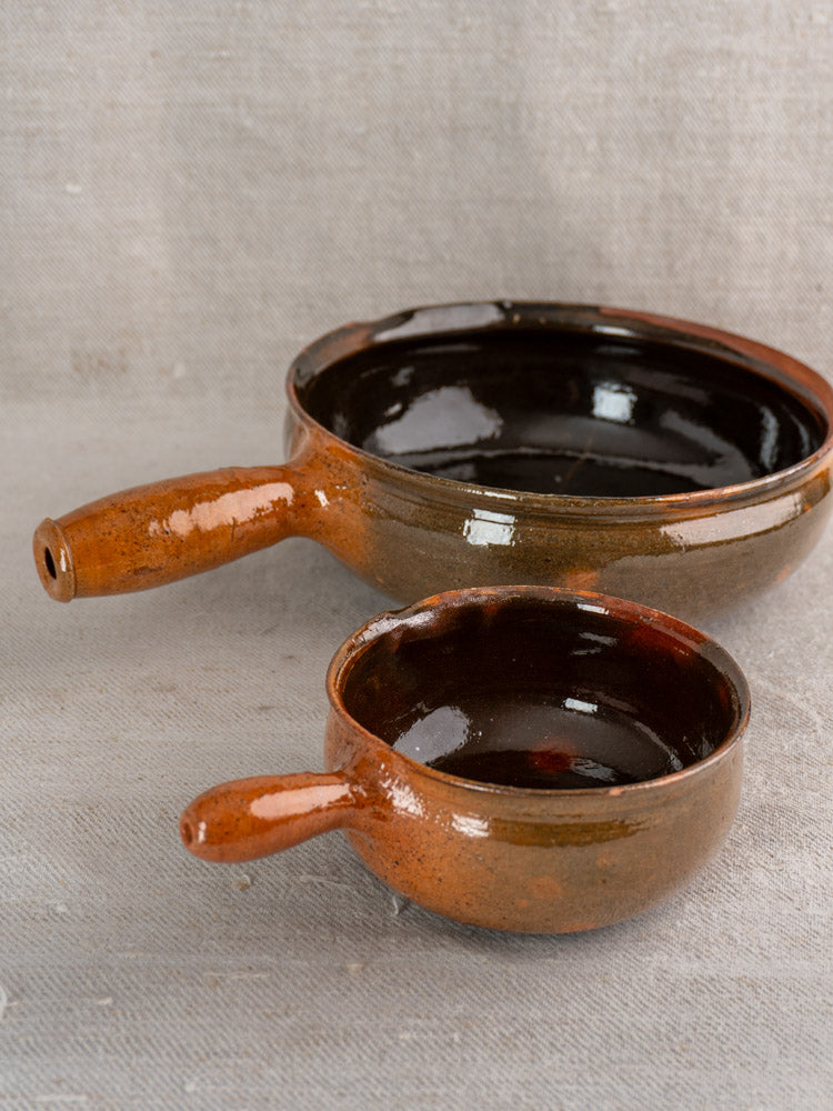 Antique French Grandjean Jourdan Vallauris poêlons, shallow pan and small saucepan with handles, on beige fabric.