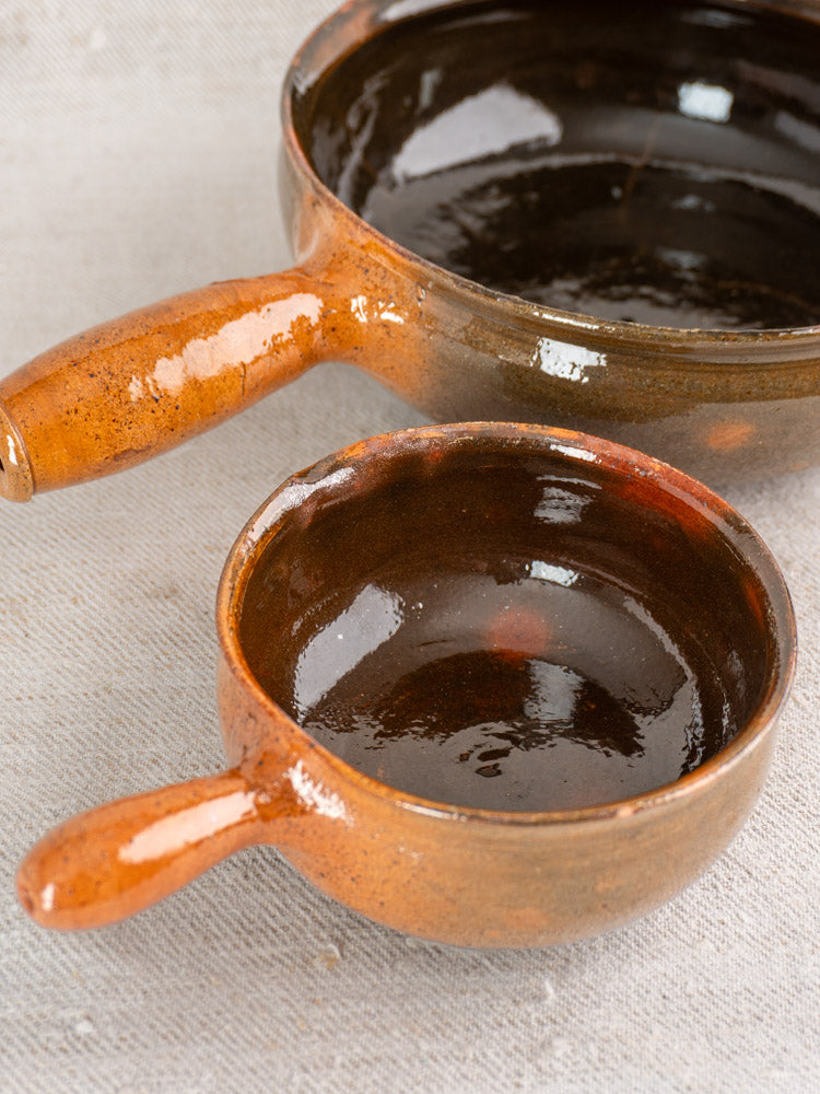 Pair of mid-century Grandjean Jourdan Vallauris French poêlon bowls with brown glaze and handles on light textured surface.