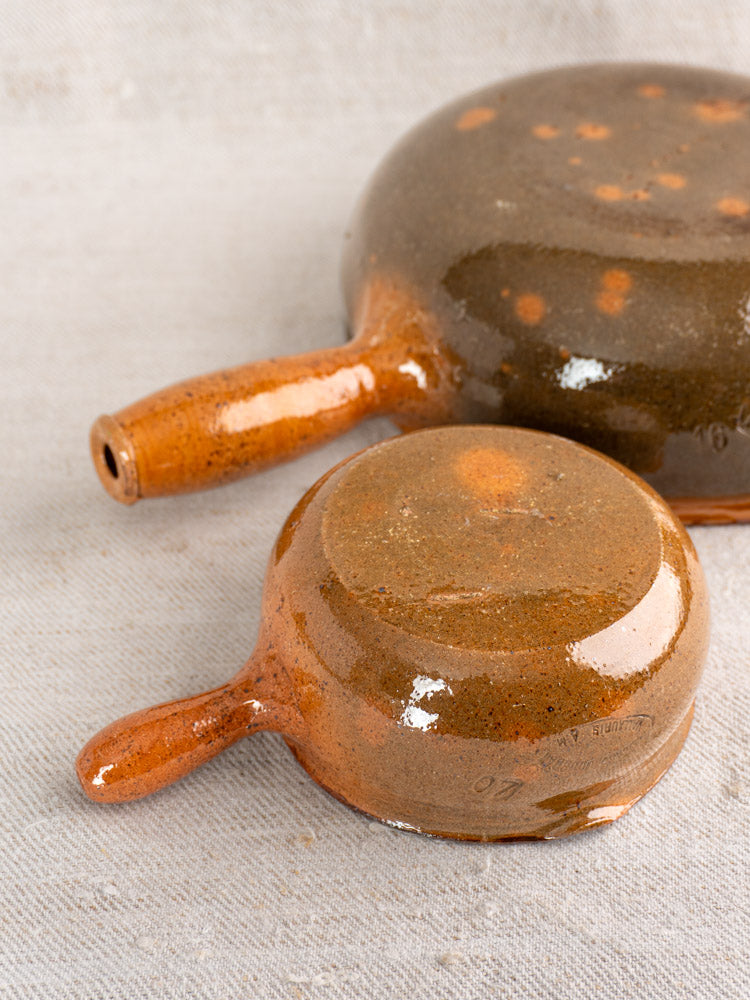Antique French poêlon pair by Grandjean Jourdan Vallauris with reddish-brown glaze, dark speckles, and classic handles.
