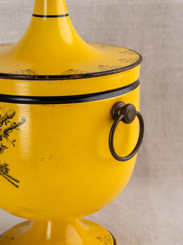 Vintage French Tôle Peinte champagne cooler in yellow Directoire style with black floral motifs, beige fabric background.