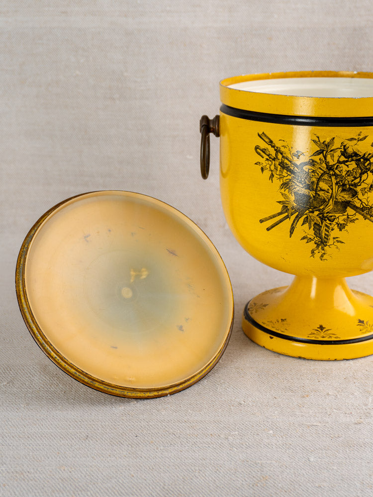 Vintage French yellow Tôle Peinte champagne cooler in Directoire style with black floral design and lid alongside.