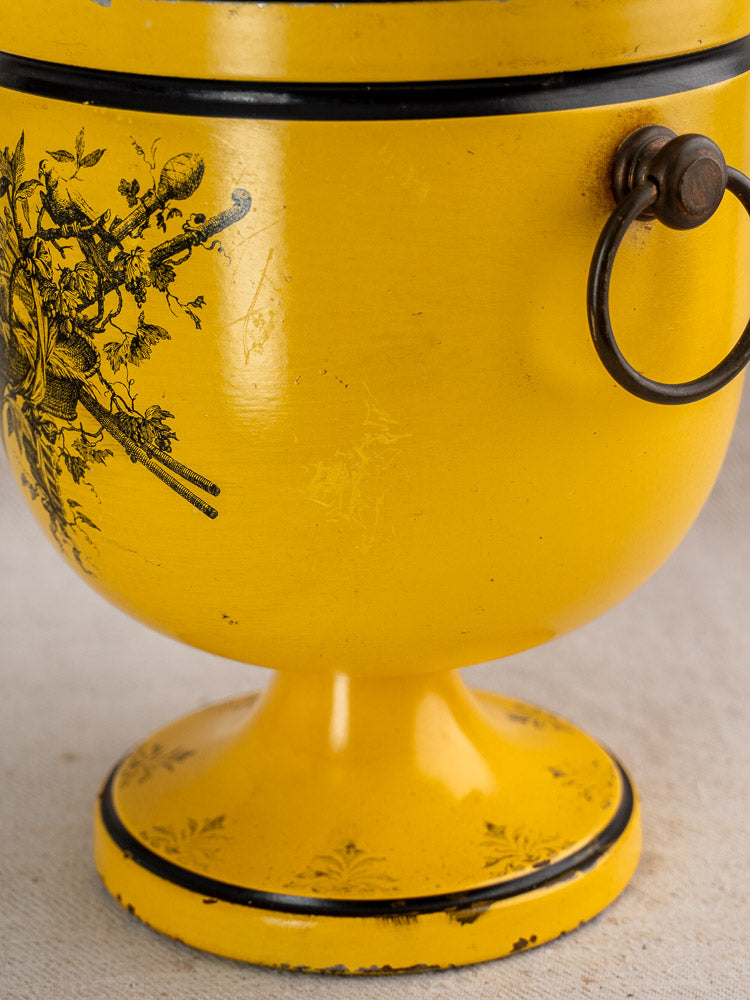 Vintage French tôle peinte champagne cooler in yellow Directoire style with black detailing, on light fabric.