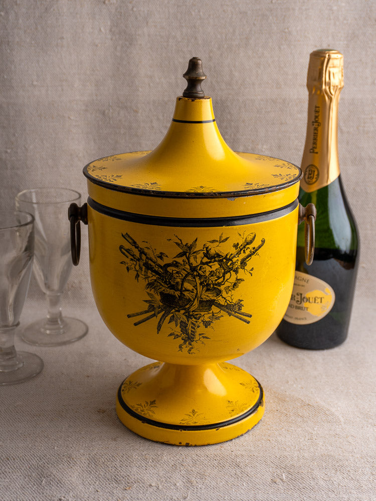 Vintage French yellow Tôle Peinte champagne cooler with floral motifs, shown with glasses and champagne bottle.