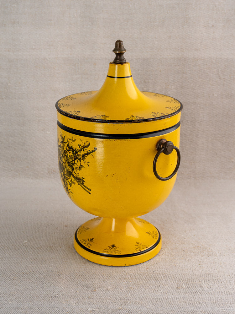 Vintage French yellow tôle peinte champagne cooler with black accents, floral motif, and round side handle on neutral fabric.